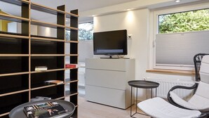 Een moderne woonkamer met een televisie, een boekenkast, een stoel en een bijzettafeltje.