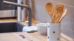 Een keuken met een houten snijplank, een metalen kraan en een witte mok met houten keukengerei.