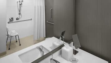 A modern bathroom with a large mirror, two sinks, a shower with a handheld showerhead, a towel rack, and a grab bar.