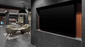 A modern interior with a large flat-screen TV mounted on a dark wall, surrounded by beige chairs and a small table. - Courtyard by Marriott Titusville Kennedy Space Center (Titusville)