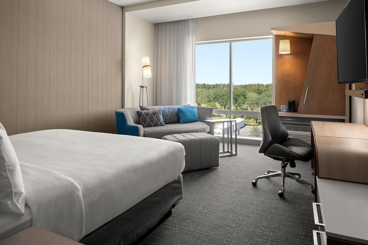 A hotel room with a large bed, a sofa, a desk, and a TV.