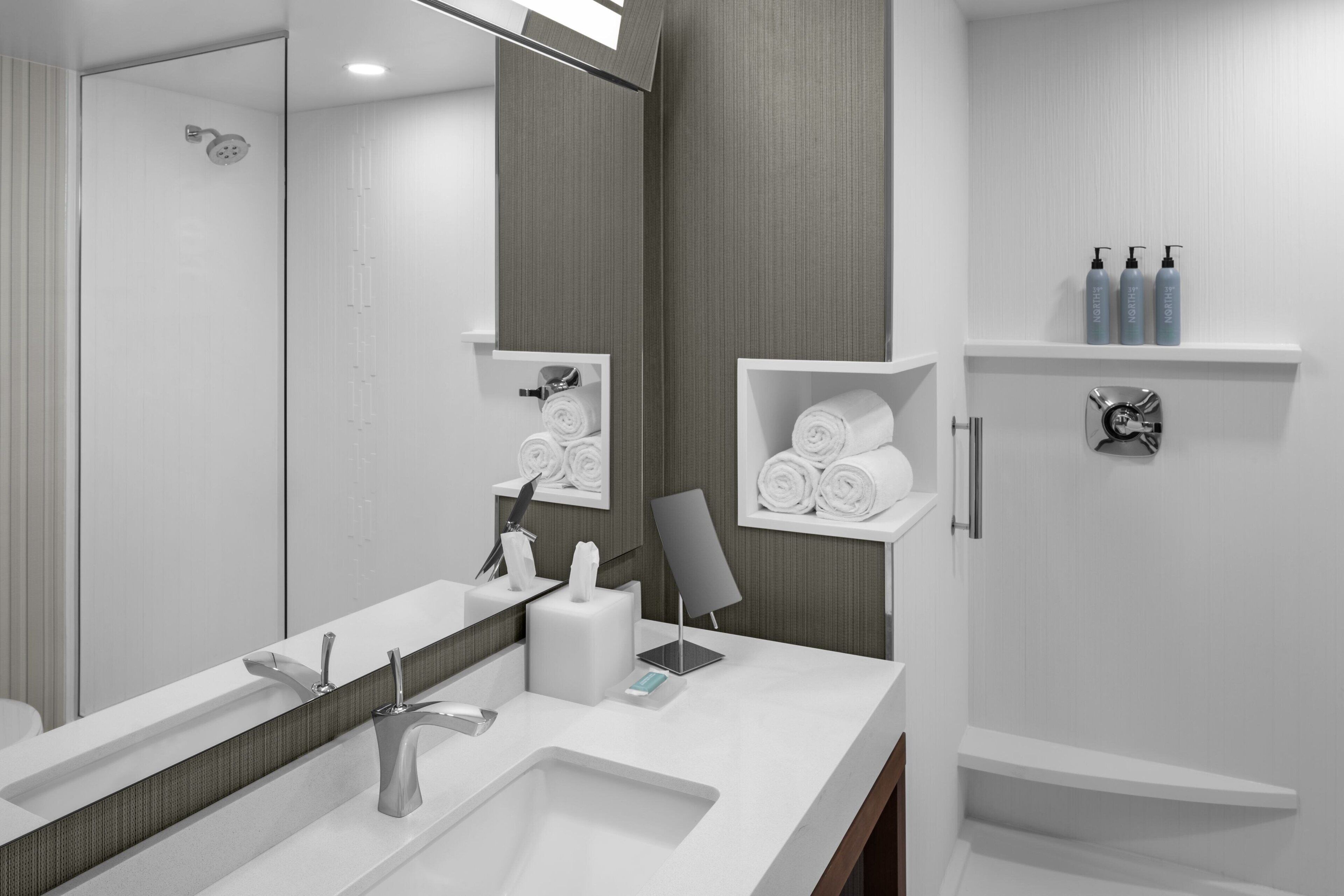 A modern bathroom with a large mirror, a sink, a shower, and shelves with toiletries.