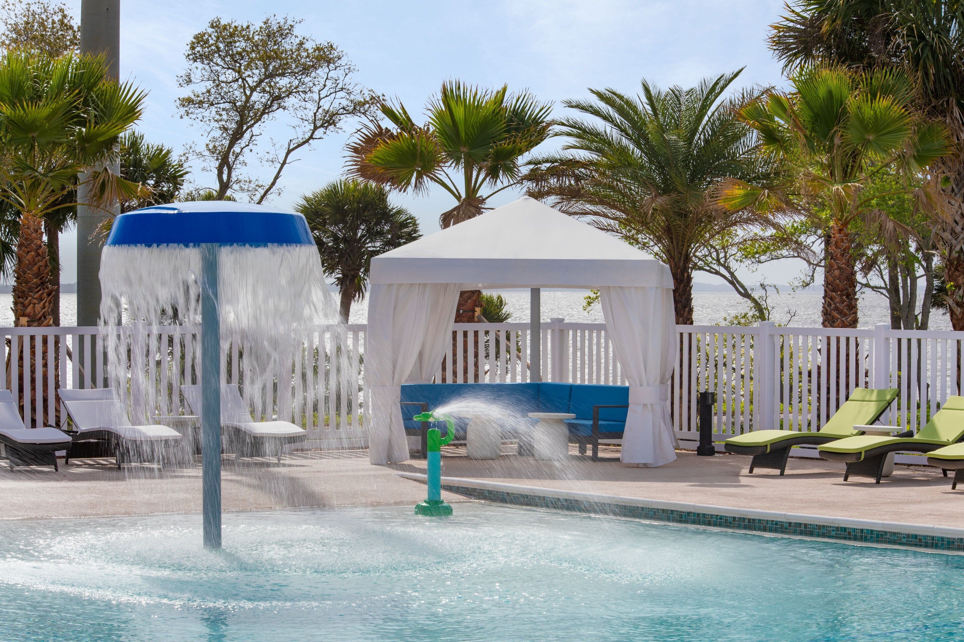 A pool area with a water fountain, lounge chairs, and a gazebo.