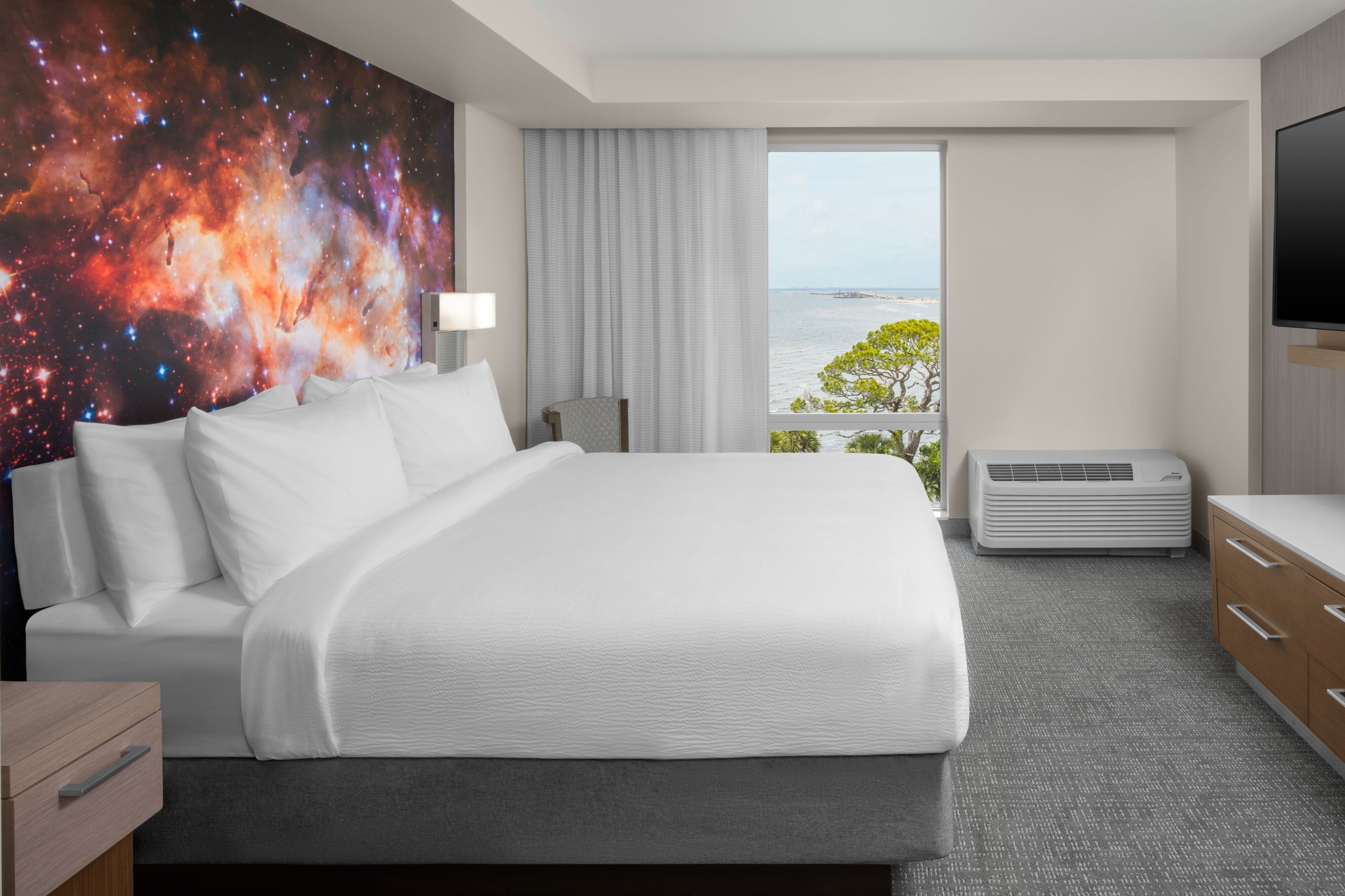 Ein Hotelzimmer mit einem großen Bett, einem Flachbildfernseher, einem Fenster mit Meerblick und einer Wand mit einem Wandgemälde zum Thema Weltraum.