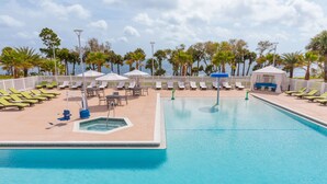 A pool area with lounge chairs and umbrellas, surrounded by palm trees and a view of the sea. - Courtyard by Marriott Titusville Kennedy Space Center (Titusville)