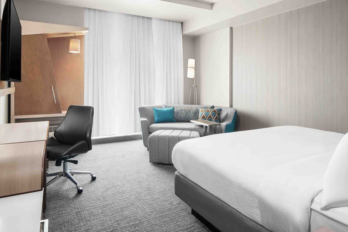 A hotel room with a bed, a desk, a chair, a sofa, and a TV.