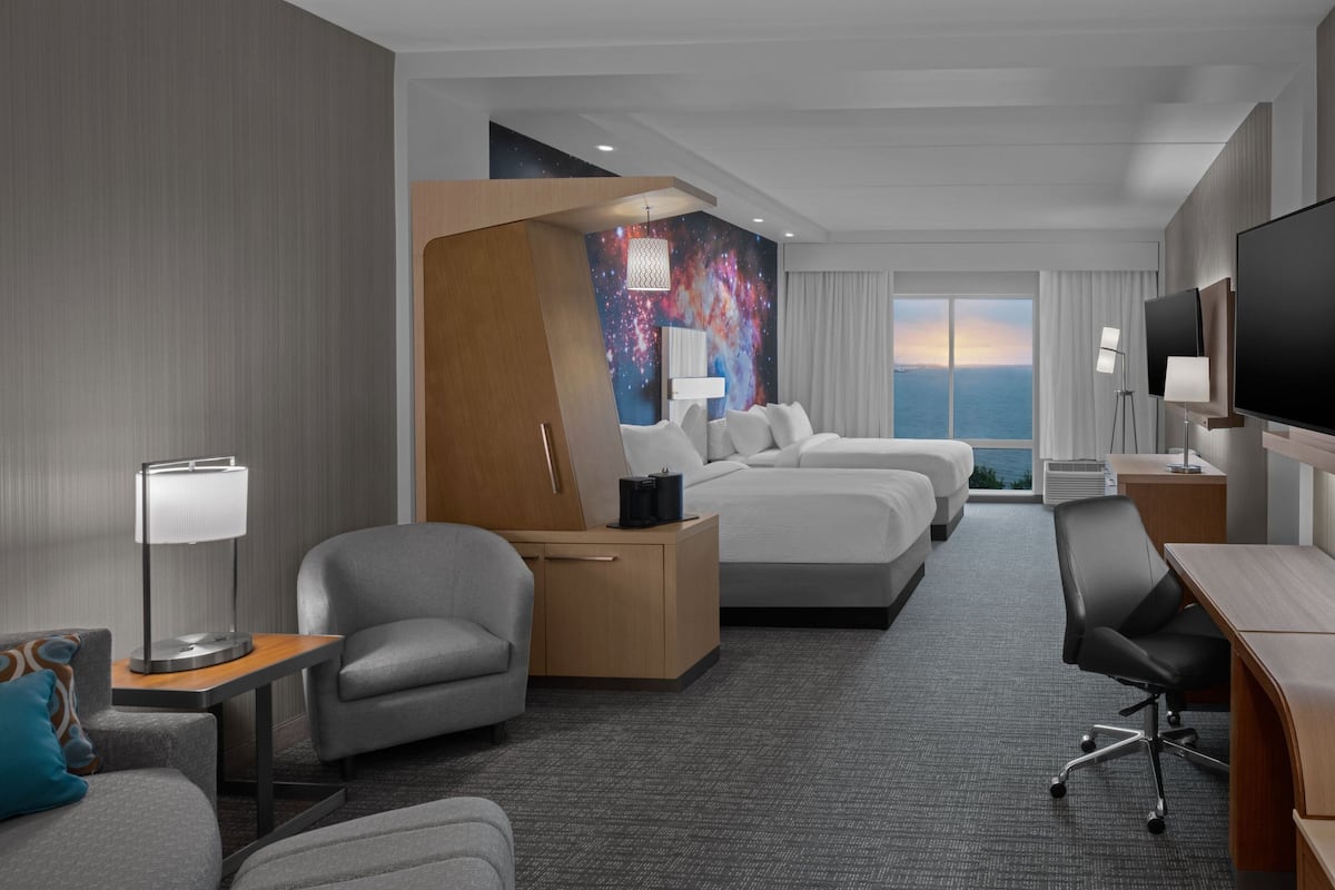 A hotel room with a large bed, a desk, a chair, a sofa, a lamp, and a TV.