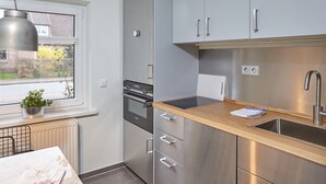 A modern kitchen with stainless steel appliances, a wooden countertop, and a window with a view of a garden. - Strandpirat - Holiday apartment for two (Sankt Peter-Ording)