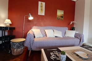 Un salon chaleureux avec un canapé à motifs, une batterie, une lampe et une petite table sur laquelle est posée une plante.
