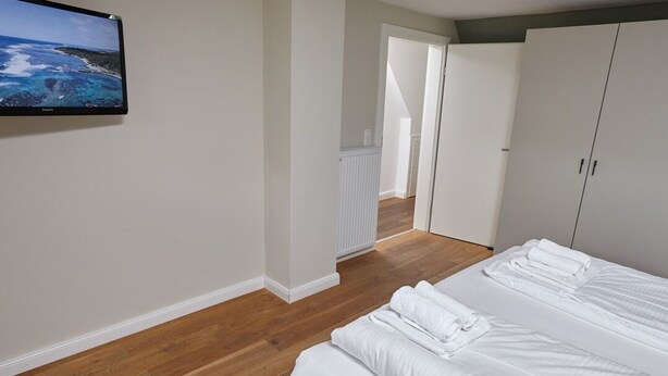 A bedroom with a large bed, a television on the wall, and a view of a coastal landscape.