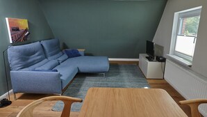 A modern living room with a sectional sofa, a wooden coffee table, and a television on a white stand.
