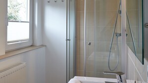 A modern bathroom with a glass-enclosed shower, a large mirror, and a window providing natural light.