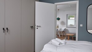 Une chambre à coucher avec un lit, une armoire blanche et une porte donnant sur un coin repas équipé d’une table et de chaises.
