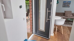 Une pièce moderne dotée d’une porte-fenêtre coulissante donnant sur un espace extérieur, avec une table blanche, un banc bleu et un canapé gris.