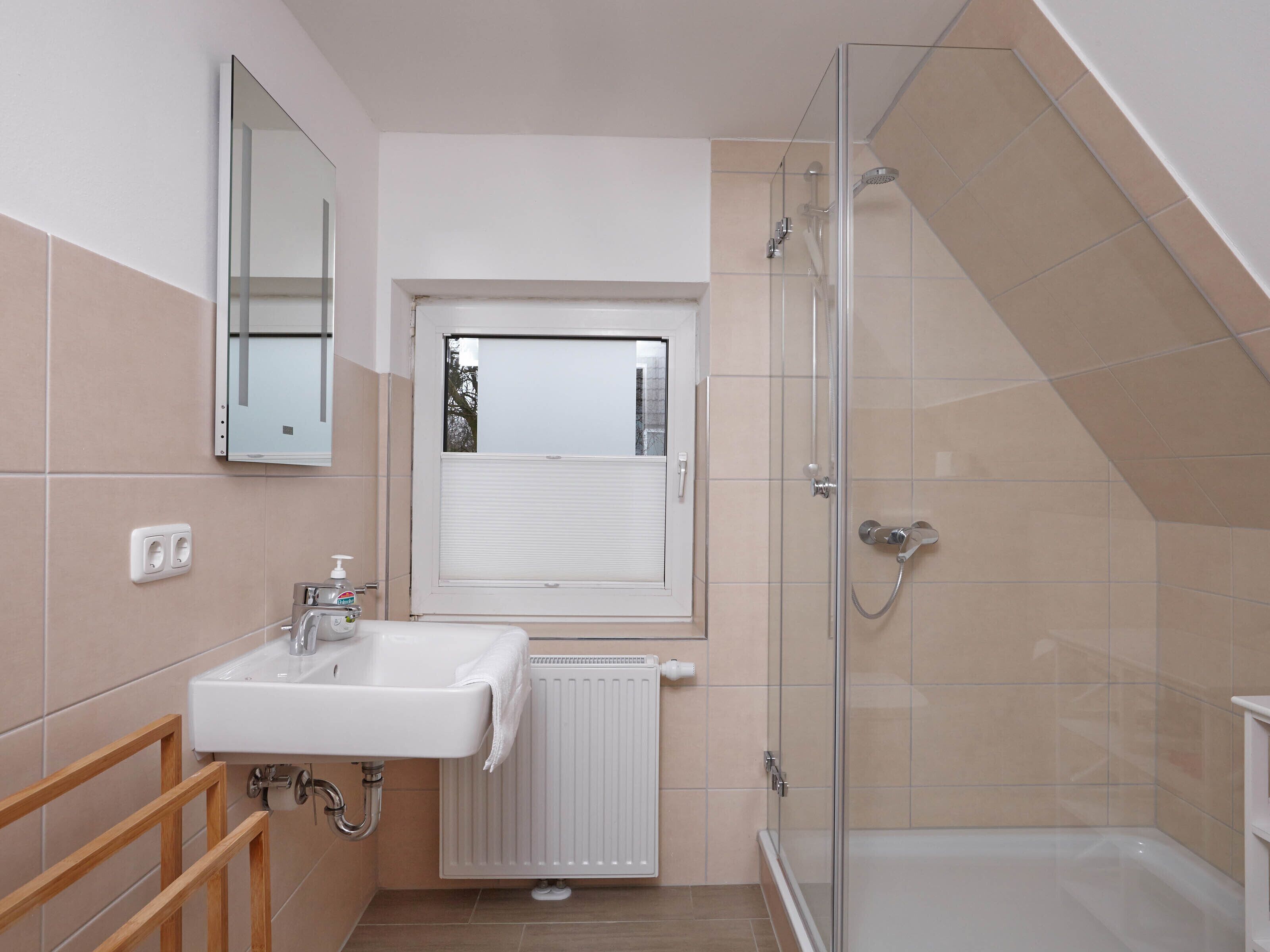 Ein modernes Badezimmer mit Waschbecken, Spiegel, Fenster, Dusche und Heizkörper.