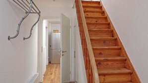 A wooden staircase with a metal handrail, a white door leading to a kitchen, and a white radiator on the floor. - Stylish vacation home Düne 10 - for up to 6 people (Sankt Peter-Ording)