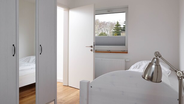 A bedroom with a bed, a bedside lamp, a window with a view, and a wardrobe. - Stylish vacation home Düne 10 - for up to 6 people (Sankt Peter-Ording)