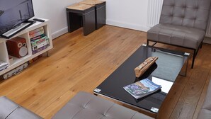 A living room with a sofa, a coffee table with a magazine, a television on a stand, and a bookshelf with board games. - Stylish vacation home Düne 10 - for up to 6 people (Sankt Peter-Ording)