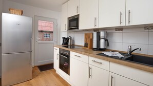 A modern kitchen with white cabinets, stainless steel appliances, a wooden countertop, and a window with a view of a brick building. - Stylish vacation home Düne 10 - for up to 6 people (Sankt Peter-Ording)
