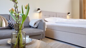 Ett modernt sovrum med en säng, ett sängbord med en vas med blommor, en soffa och två väggmonterade lampor.