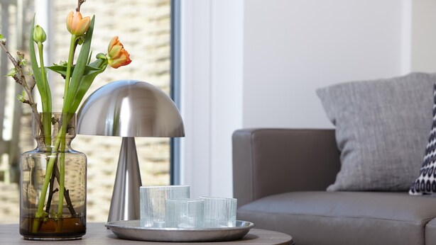 Ett modernt vardagsrum med ett runt soffbord, en vas med blommor och en lampa.