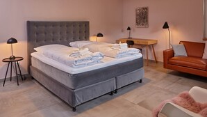 A bedroom with a large bed, bedside tables, a desk, a chair, and a painting on the wall. - Oystercatcher - Holiday cottage for two (St Peter Ording)