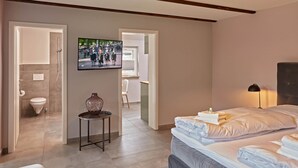 A modern hotel room with a large bed, a TV on the wall, and a bathroom visible through an open door. - Oystercatcher - Holiday cottage for two (St Peter Ording)