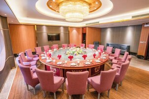 Un salón de conferencias con una mesa redonda, sillas rosadas y un candelabro.