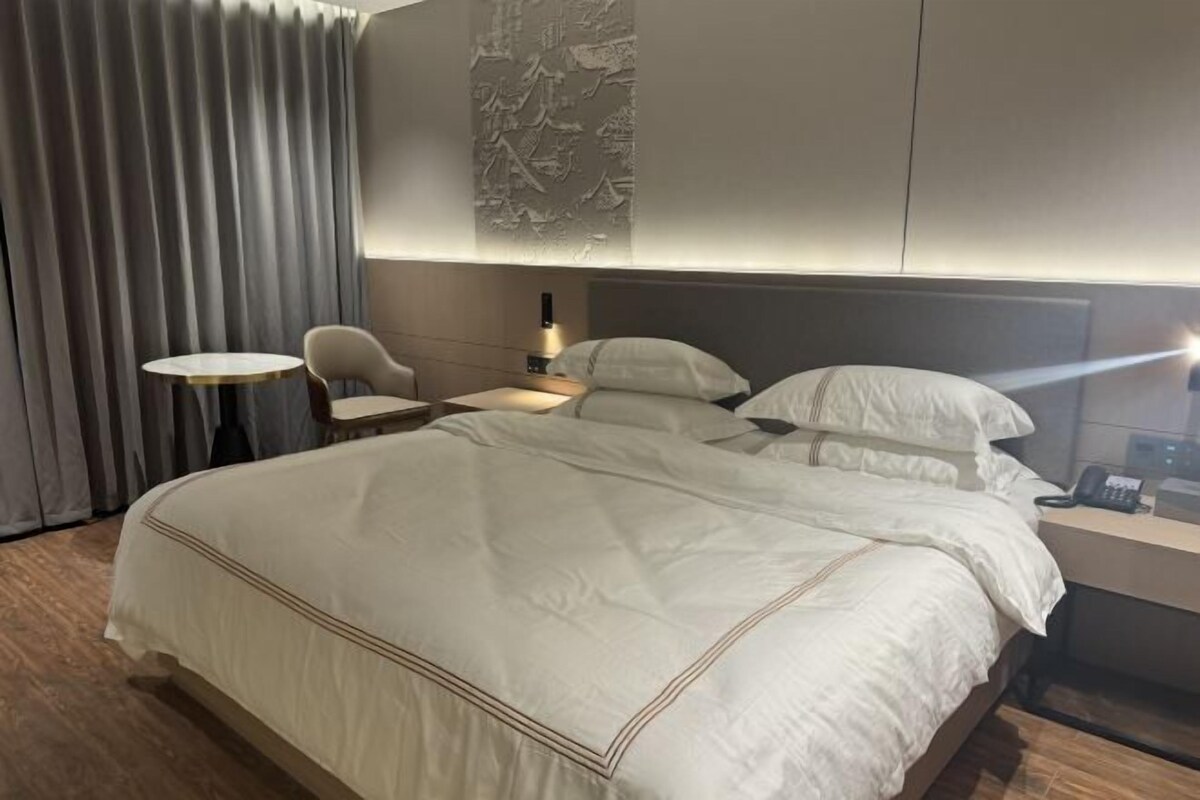 A hotel room with a large bed, a bedside table with a lamp, a chair, and a wall with a textured design.