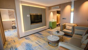 A modern hotel room with a large flat-screen TV, a sofa, a coffee table, and a patterned carpet. - Jingyang Hotel (Yingshan)