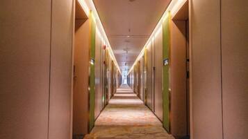 Corredor de hotel com portas em ambos os lados, carpete estampado e iluminação no teto.