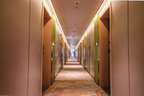 A hotel corridor with doors on both sides, a patterned carpet, and overhead lighting.