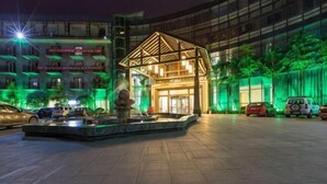 A hotel entrance with a modern design, a fountain, and a parking area with cars. - Jingyang Hotel (Yingshan)