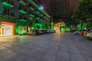 A parking area with multiple cars, a building with a green-lit facade, and a tree in the foreground. - Jingyang Hotel (Yingshan)