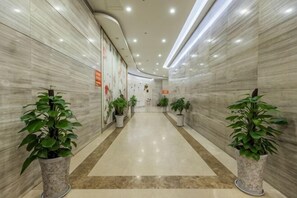 A hallway with marble walls, potted plants, and a tiled floor. - Jingyang Hotel (Yingshan)
