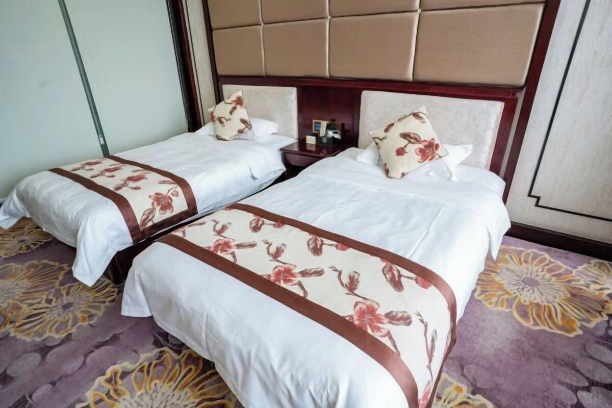 A hotel room with two beds, a headboard, a nightstand, and a floral carpet.