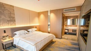A hotel room with a bed, bedside table, and a bathroom with a mirror and sink. - Jingyang Hotel (Yingshan)