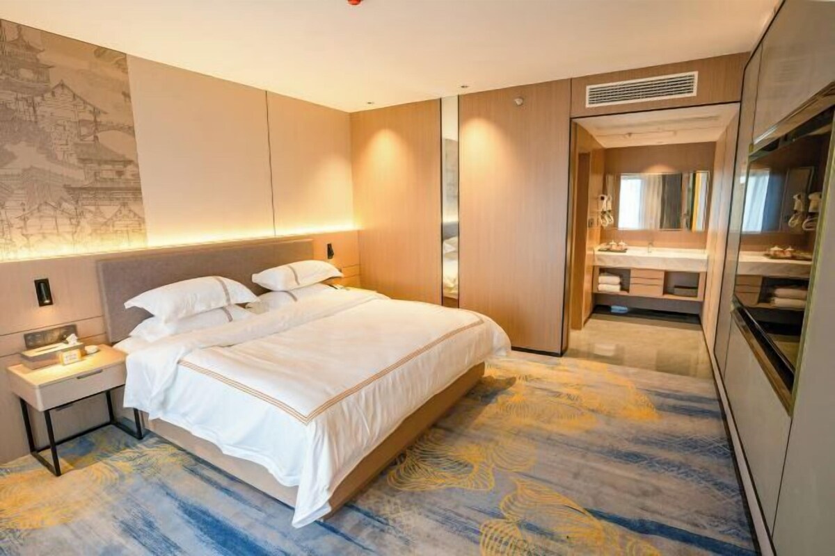 A hotel room with a bed, bedside table, and a bathroom with a mirror and sink.