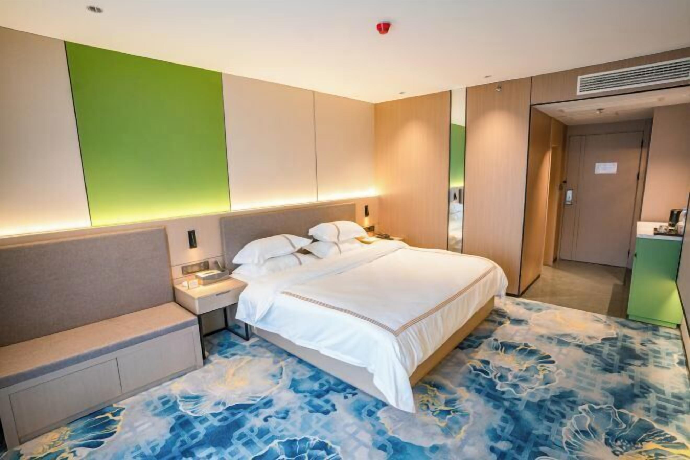 Habitación de hotel con cama, mesitas de noche, una pared de acento verde y alfombra estampada.