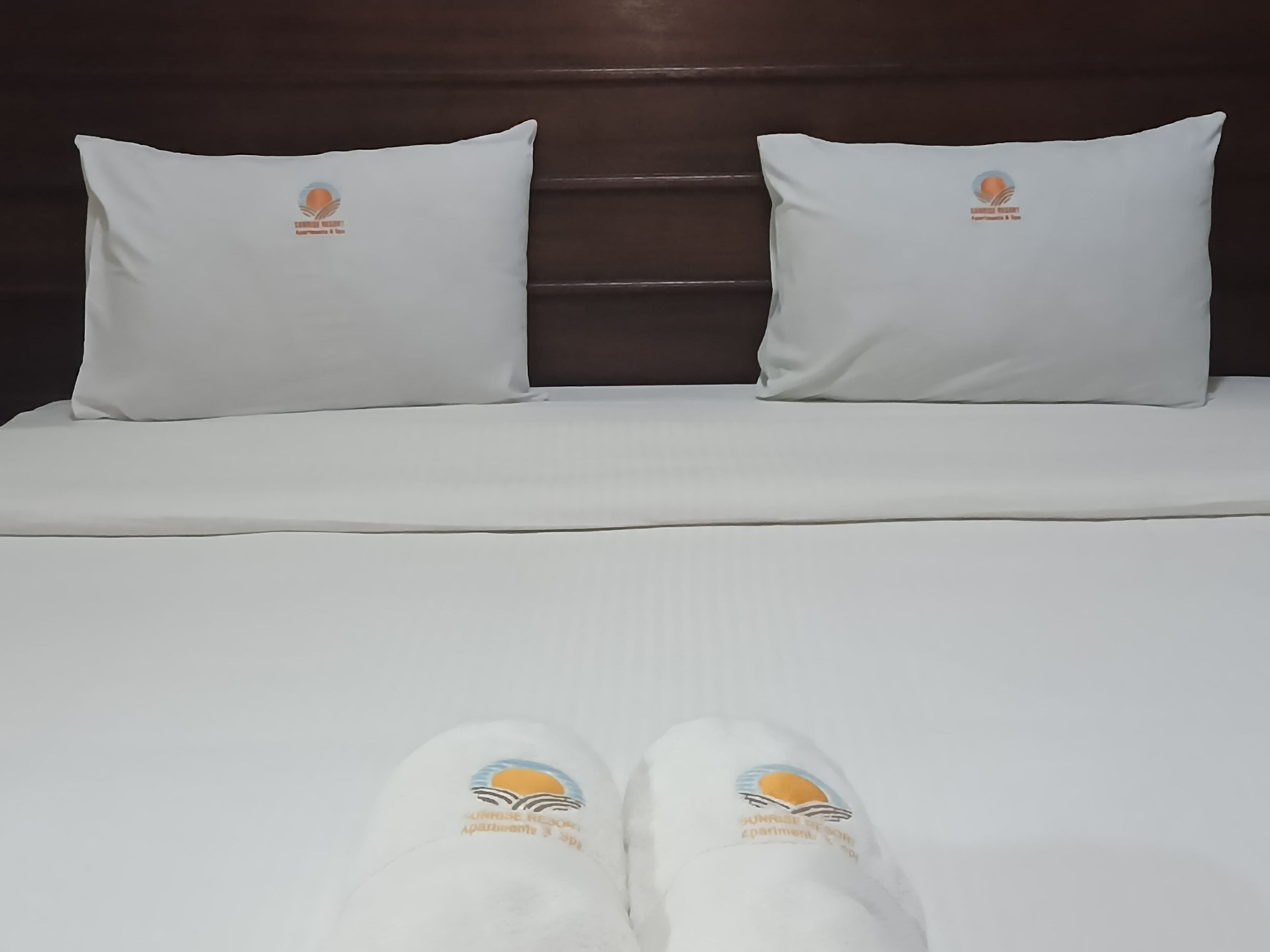 Un letto con due cuscini e un paio di ciabatte.