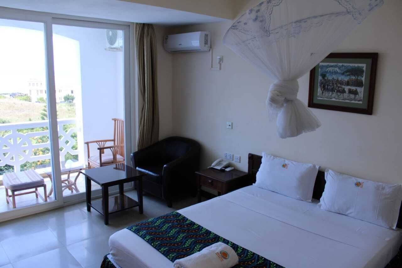 A hotel room with a bed, a desk, a chair, a bedside table with a phone, and a picture on the wall.