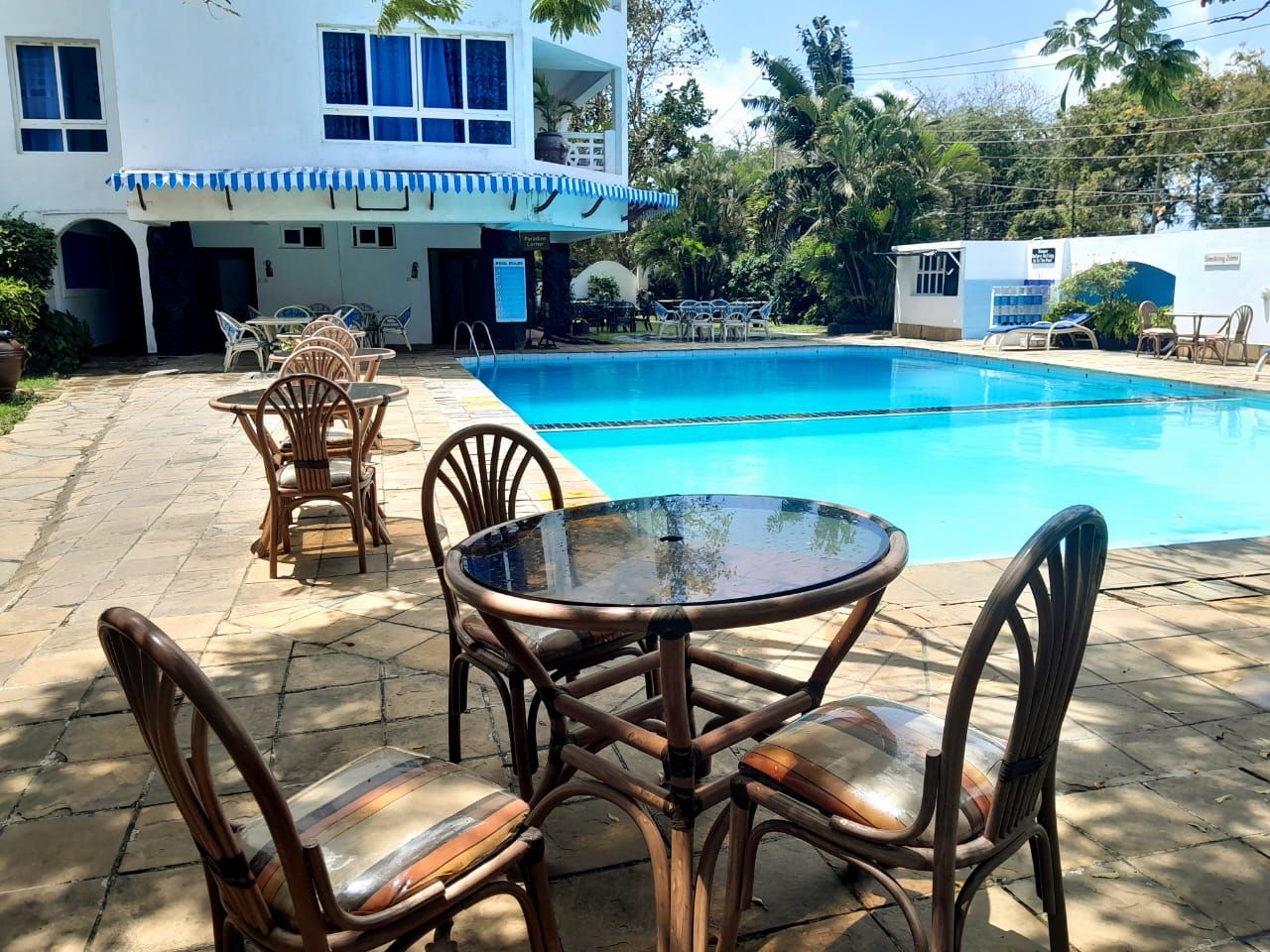A pool area with a table and chairs, a building with a balcony, and a tropical garden.