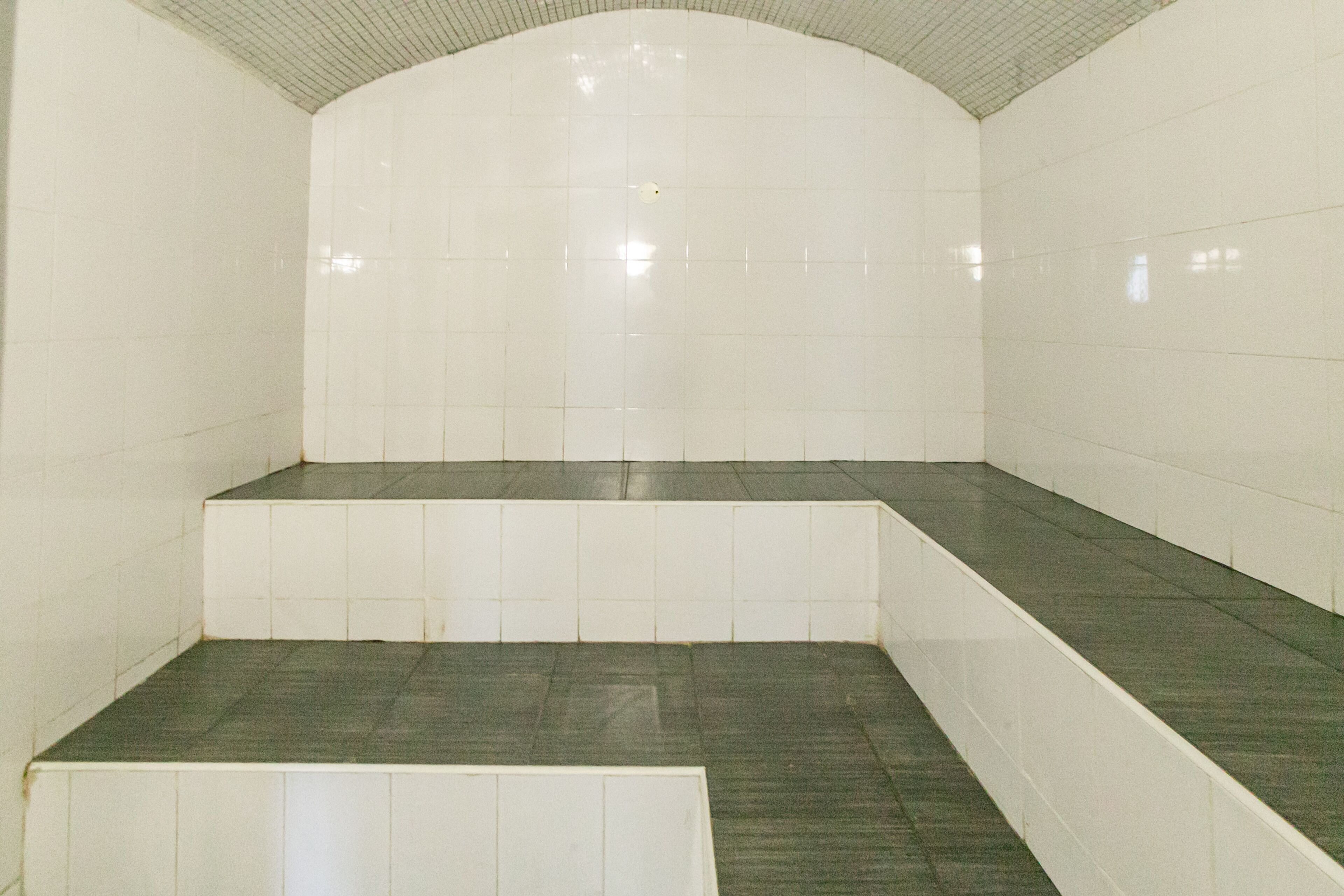 Une salle de bain carrelée avec un plafond incurvé, un sol carrelé et un banc.