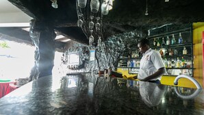 Zona de bar con mostrador de granito pulido, lámparas colgantes y estanterías llenas de botellas.