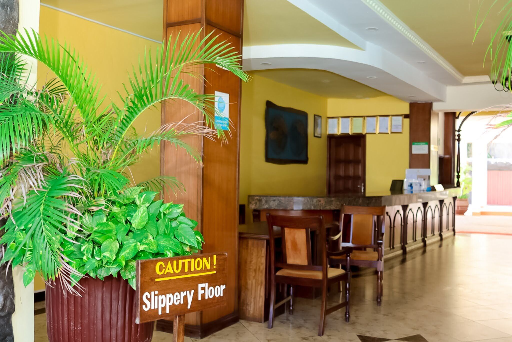 A reception area with a caution sign for a slippery floor, wooden furniture, and a plant.