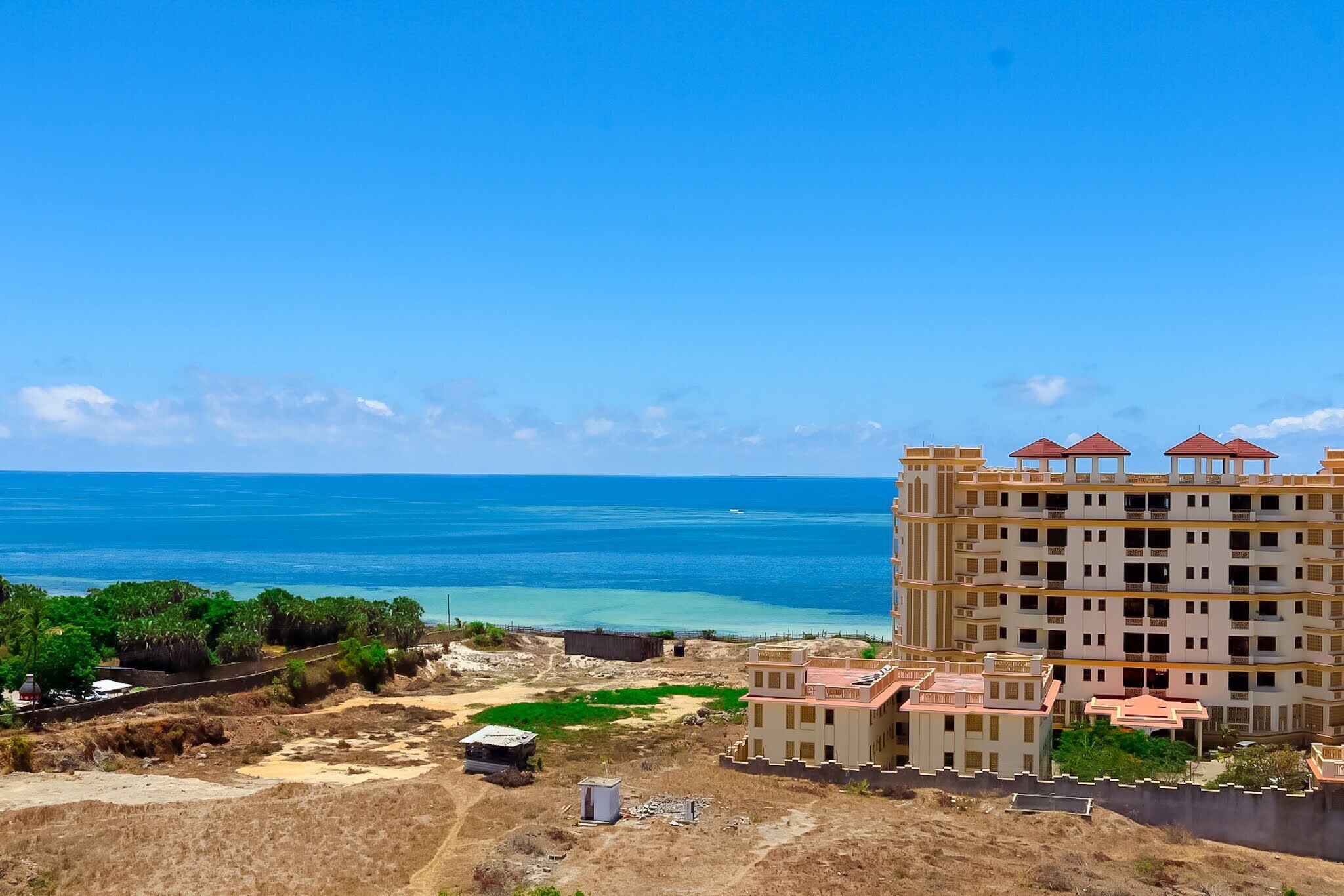 A coastal hotel with a view of the sea, a large building with multiple balconies, and a landscaped area with greenery.