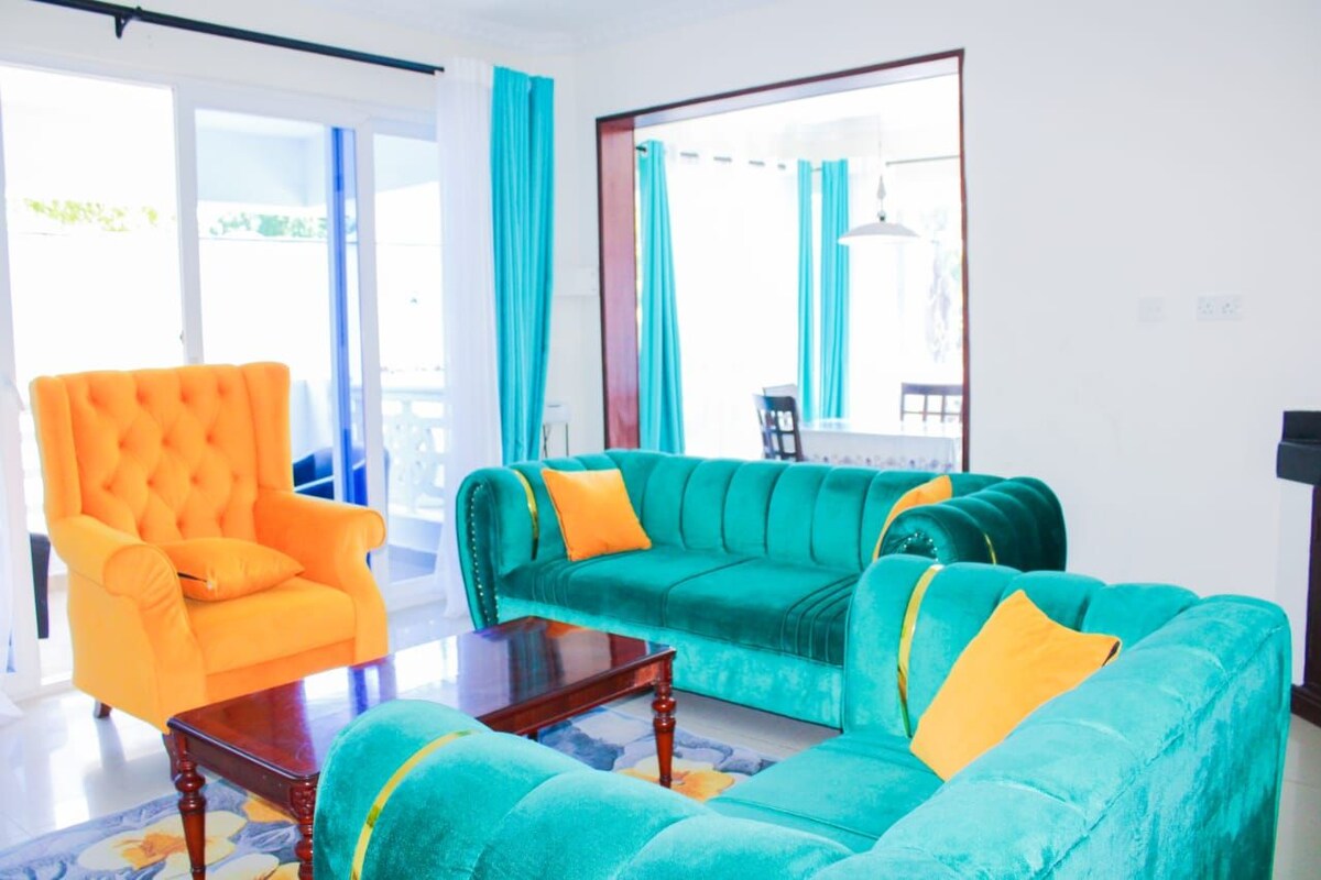 A living room with a bright orange armchair, a teal sofa with yellow cushions, and a wooden coffee table.