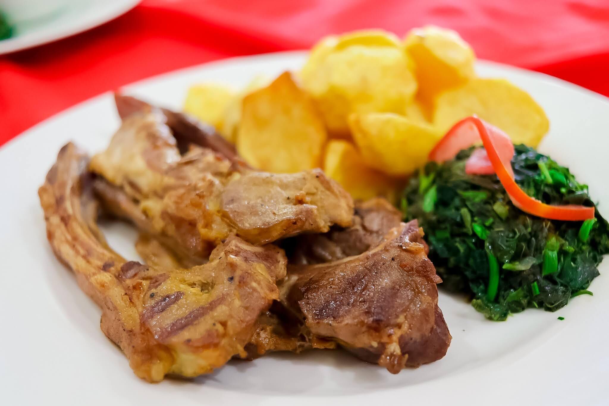 A plate with grilled meat, fried plantains, and a side of greens.