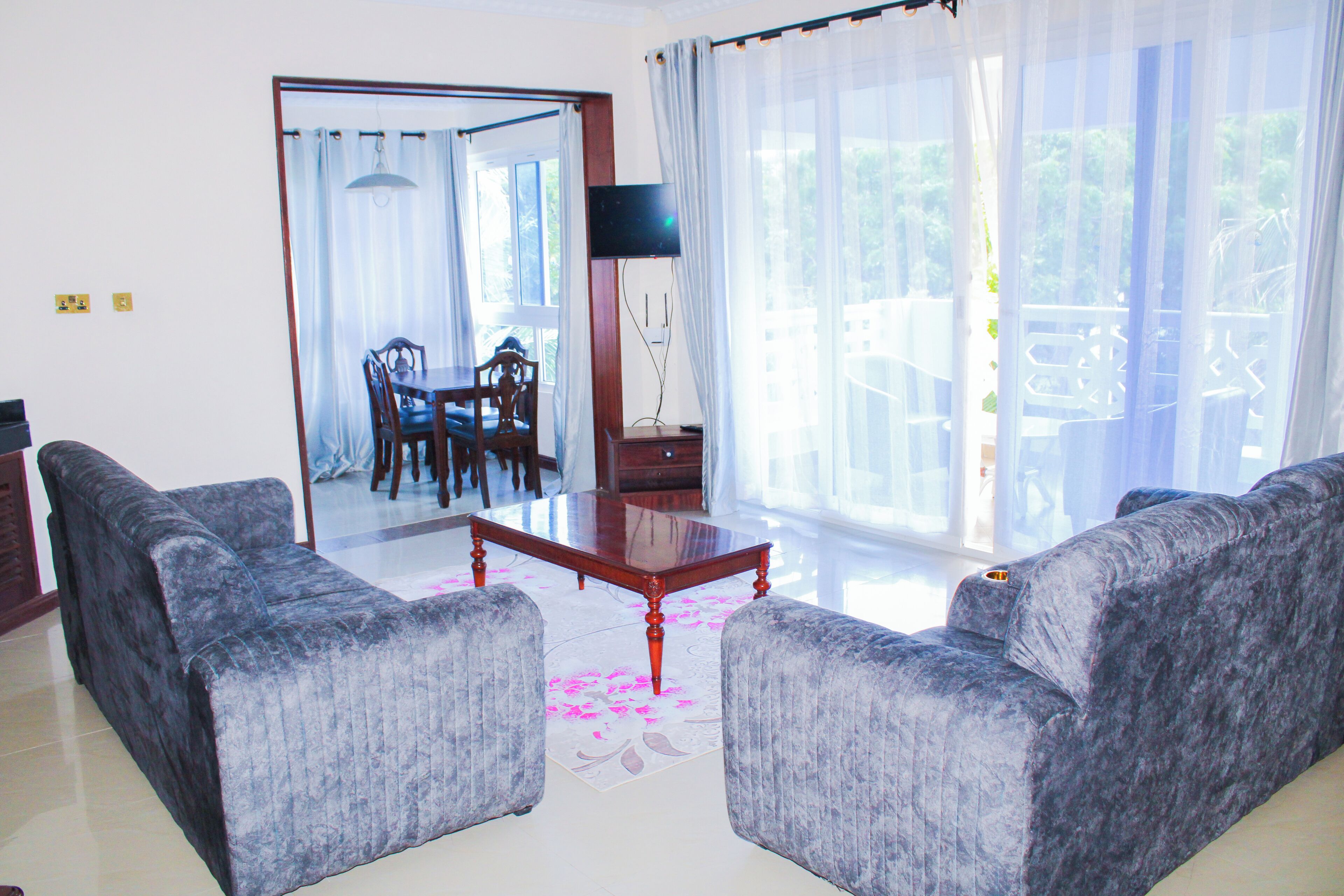 A living room with a sofa set, a dining table with chairs, a TV, and a view of the outdoors.