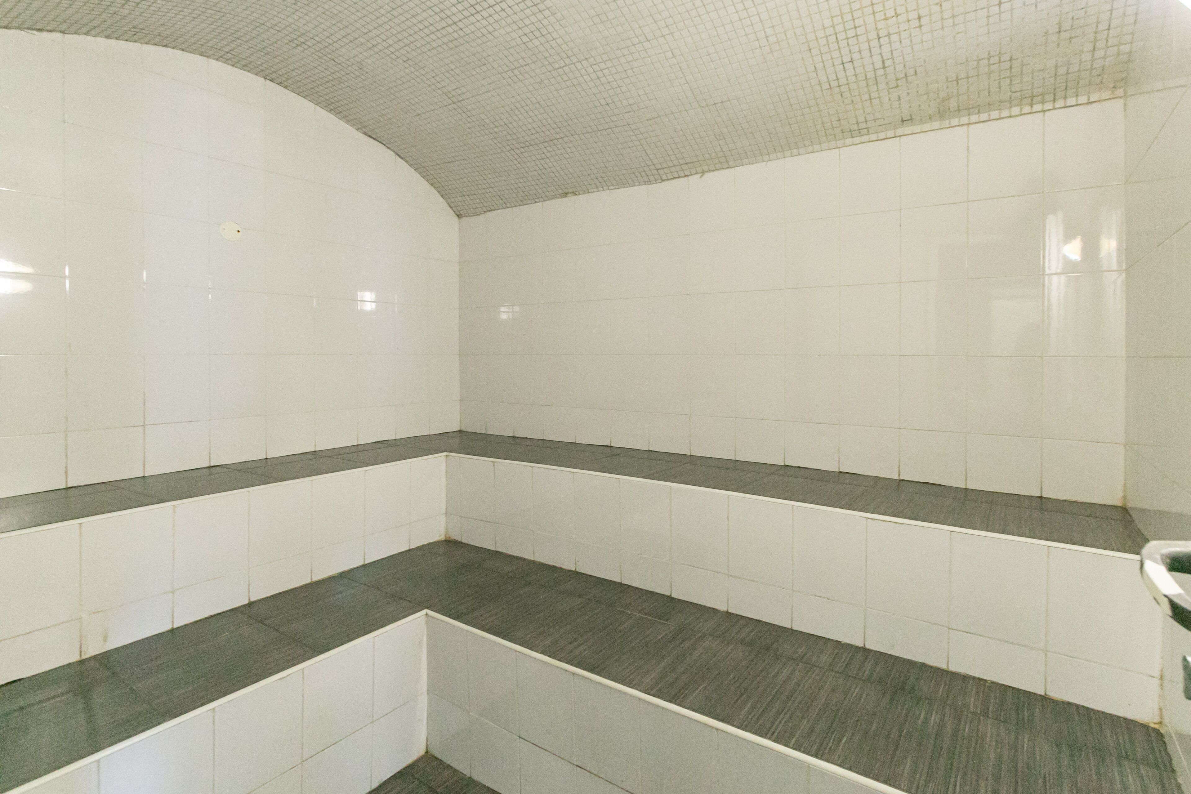 A bathroom with white tiled walls and a curved ceiling, featuring a dark grey countertop.
